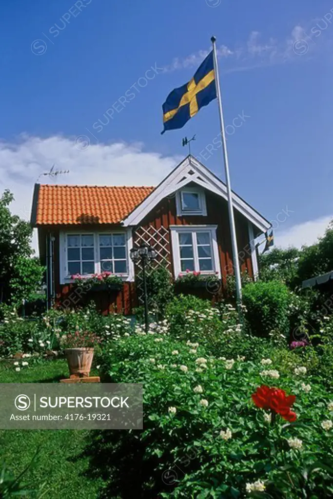 A red cottage with Swedish flag and flower bed
