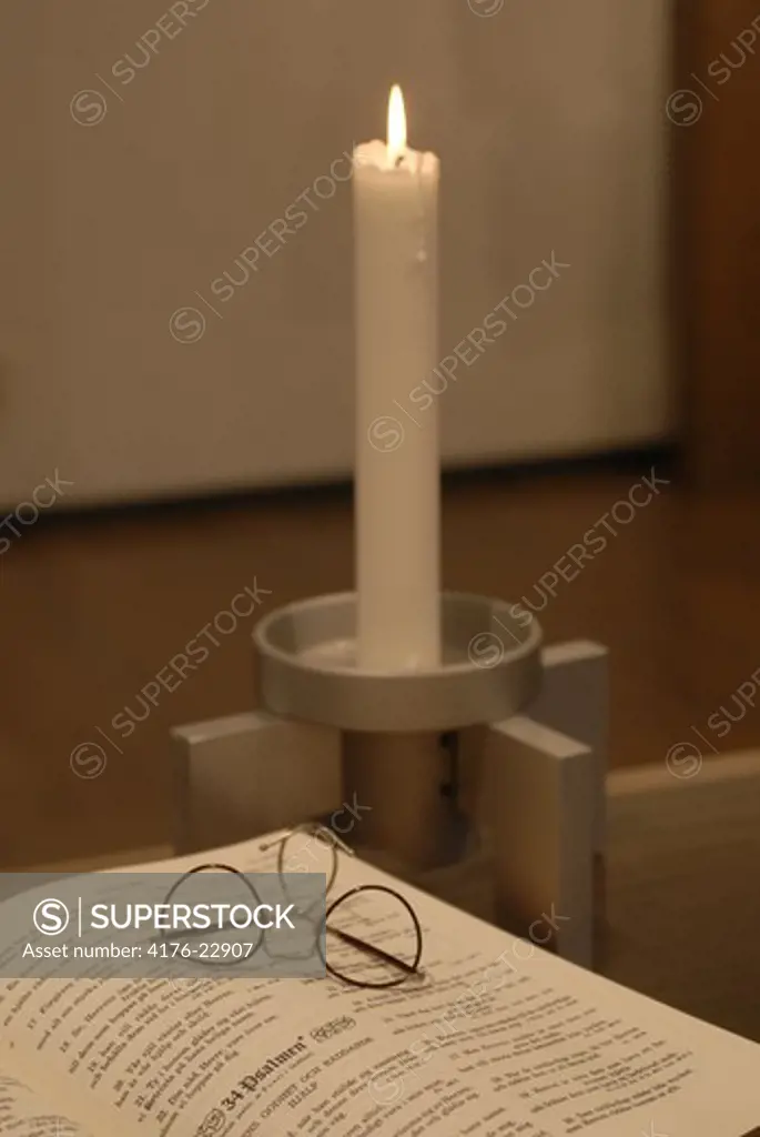 Lit candle by the eyeglasses on a book