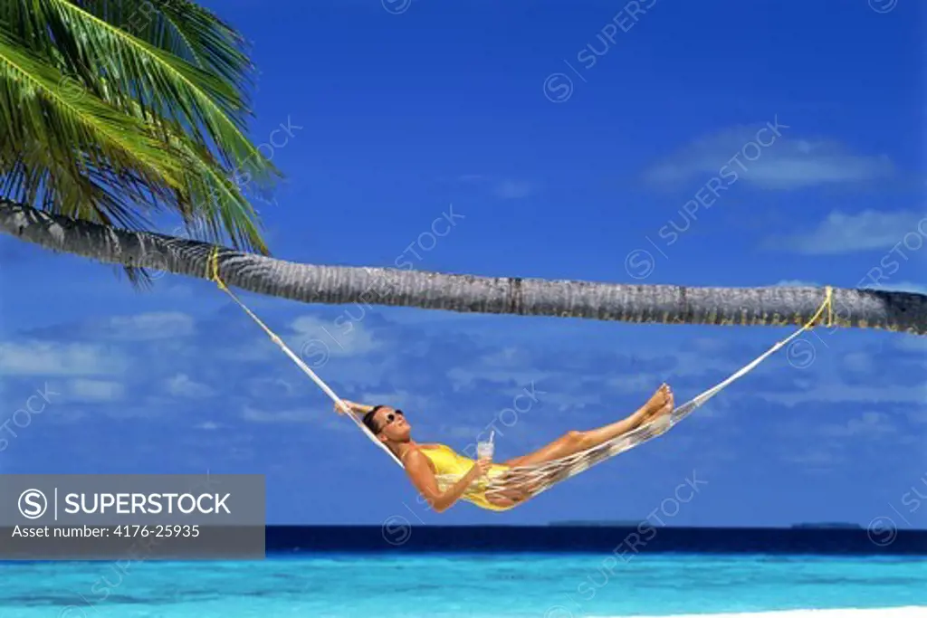 Woman relaxing in hammock under palm tree with tropical drink
