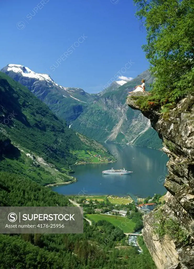 Woman sitting at Flydalsjuvet above Geiranger Fjord with passenger ship