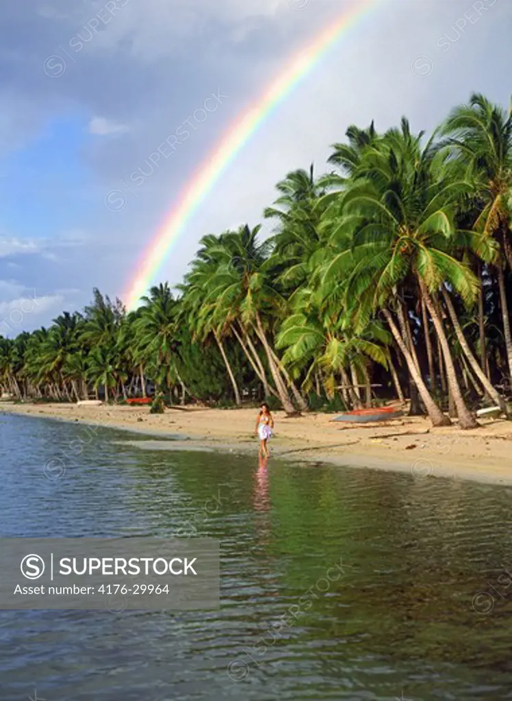 Polynesian woman walking under rainbow and palm trees on Aitutaki beach in Cook Islands