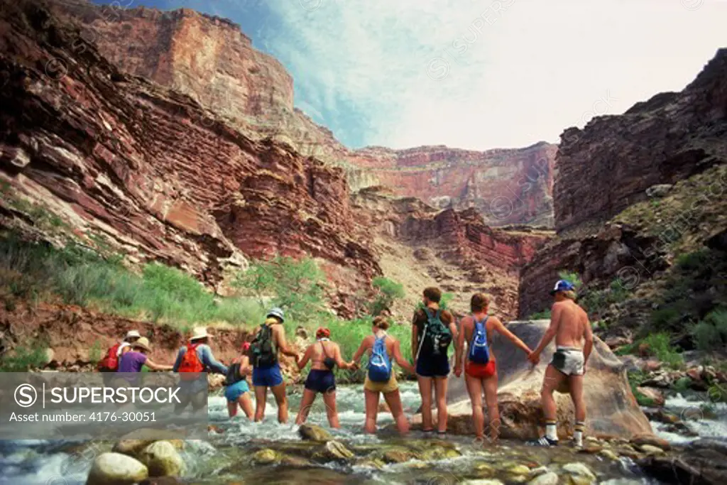 Tourists helping eachother cross Tapeats Creek inside the Grand Canyon during Colorado River rafting trip