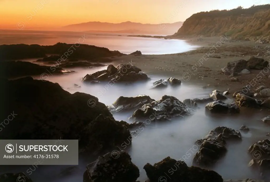 Waves painting rocky shore at sunset at Big Sur California