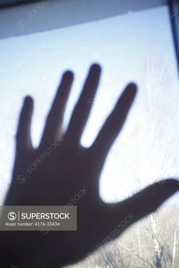 Silhouette of a left hand and fingers touching a window from the inside.
