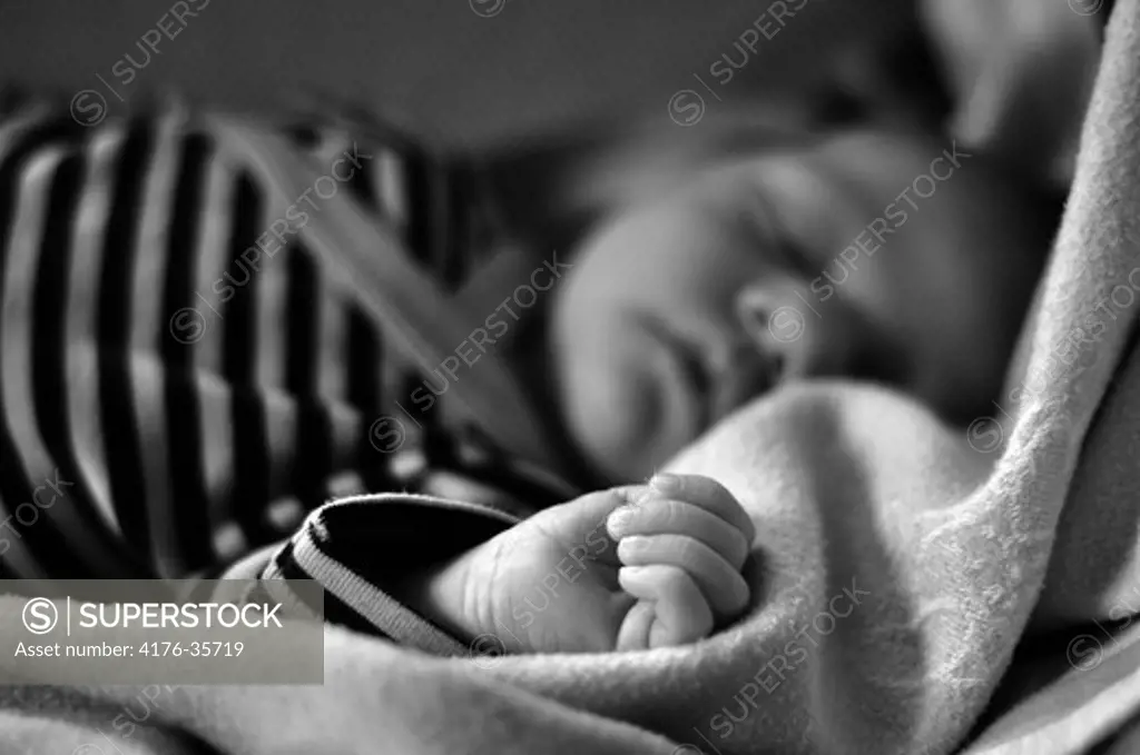 Black and white picture of newborn baby sleeping with specific focus on her small hand