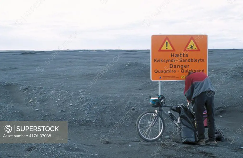 Rear view of a mountain biker standing near a warning sign, Iceland
