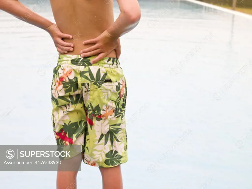 Boy standing with arms akimbo at the poolside, rear view, midsection, Iceland
