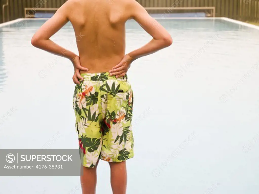 Boy standing with arms akimbo at the poolside, rear view, midsection, Iceland