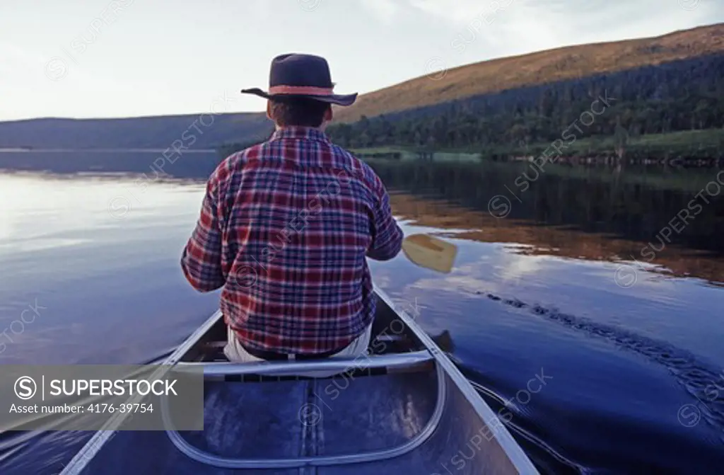 The back of a man paddling a canoe