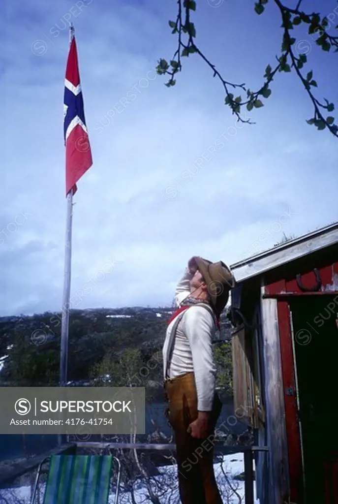 A man saluting the Norwegian flag, mountains and a cabin in background