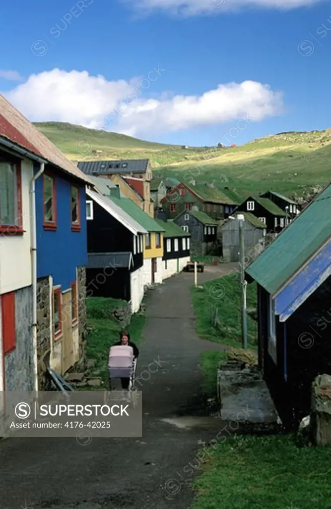 A woman with a baby carriage walking up a road in a little village in Faroe Islands.