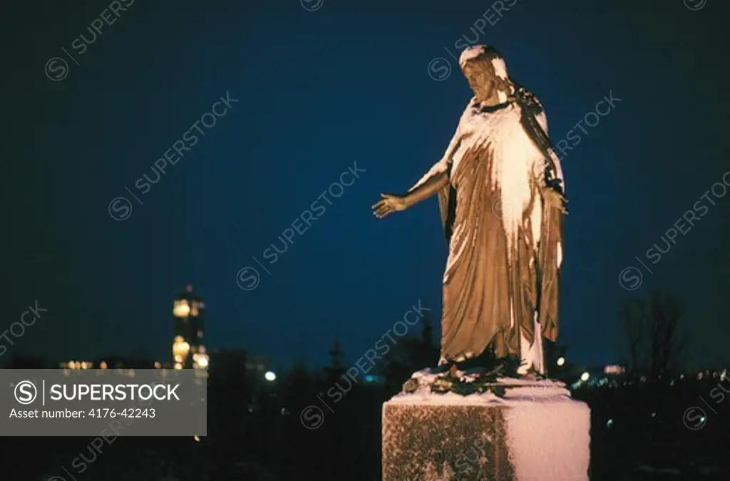 A statue of Jesus Christ with city lights in the ba