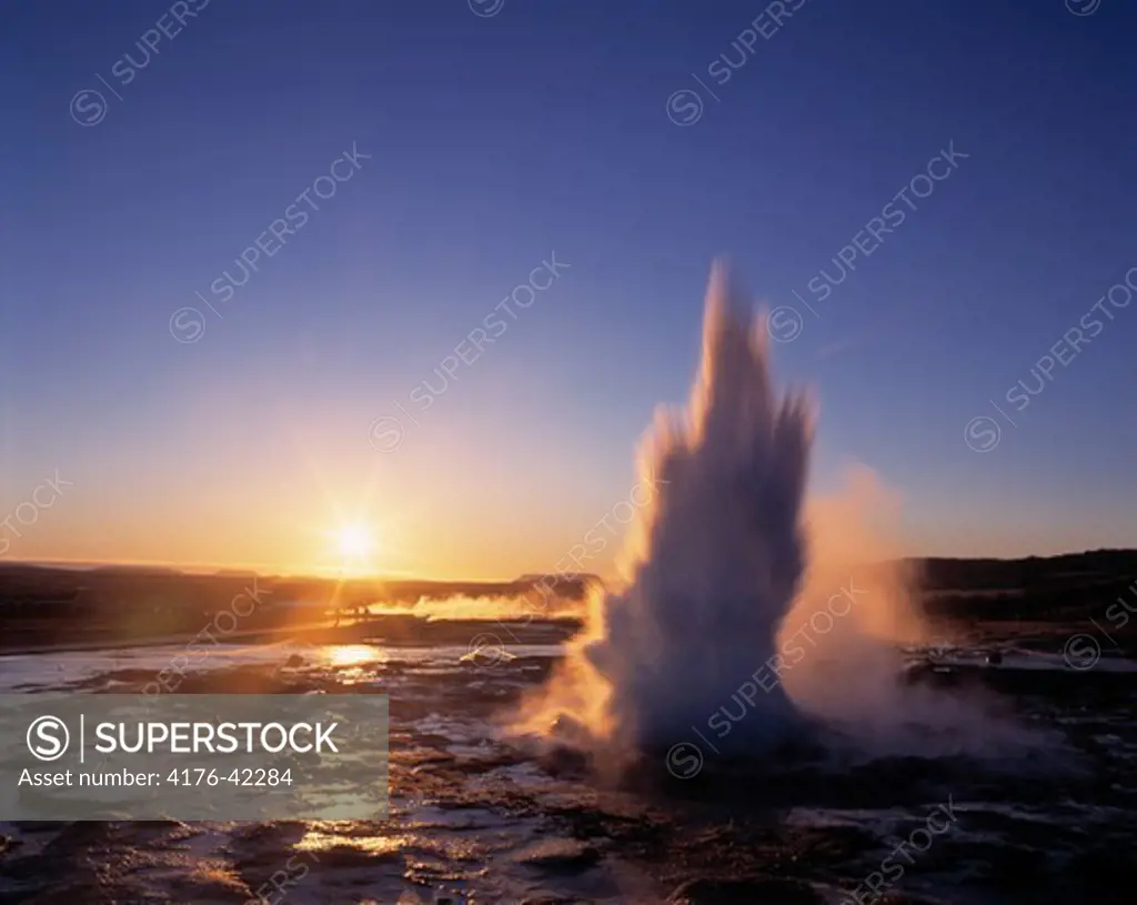 An erupting geyser at wintertime with sun going down in background, Iceland