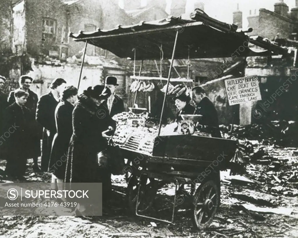 People line up to buy food from a cart amidst ruins