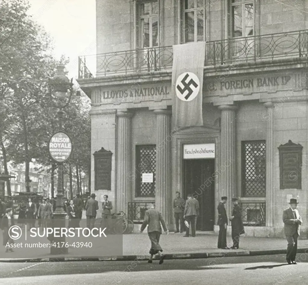 People walking in front of bank with nazi flag hung over it's doorway