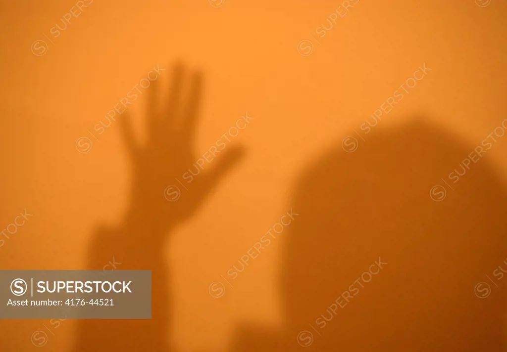 Shadow of hand and head cast on orange lit wall, Copenhagen, Denmark.