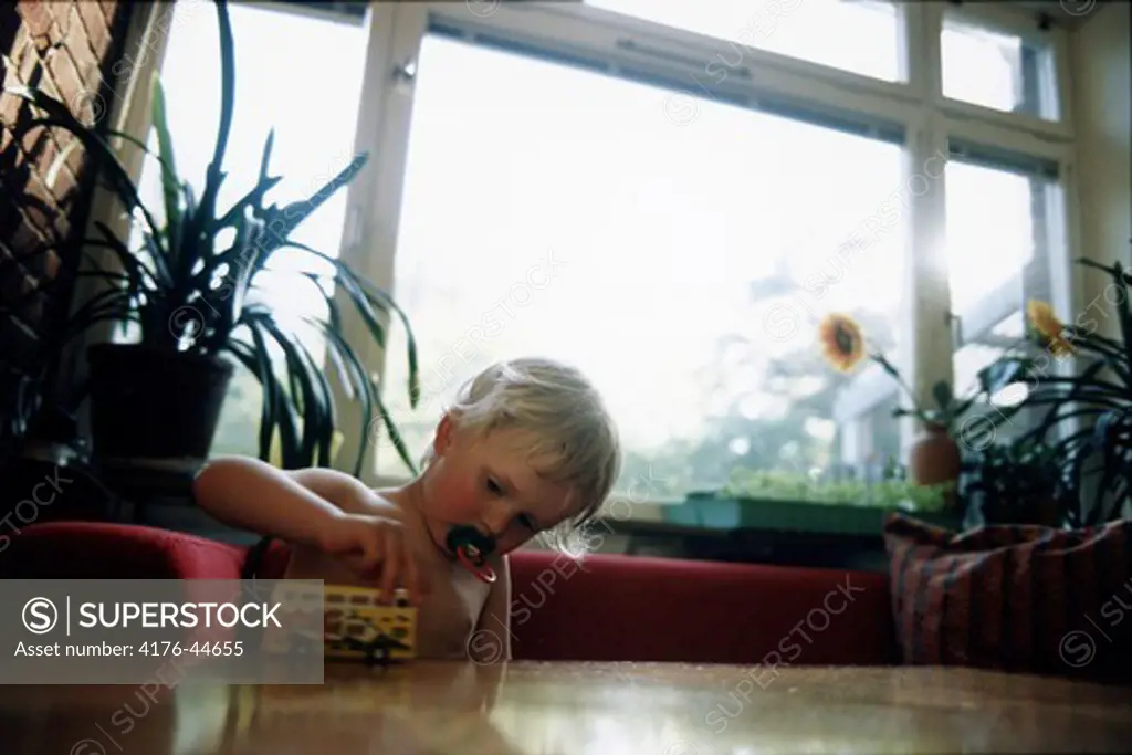 A child playing with toy bus and using pacifier