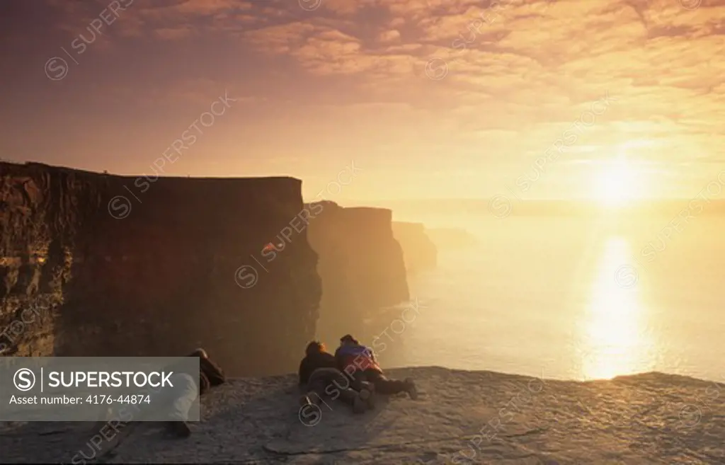 People on the cliff edge near sea and cloudy sky at sunrise