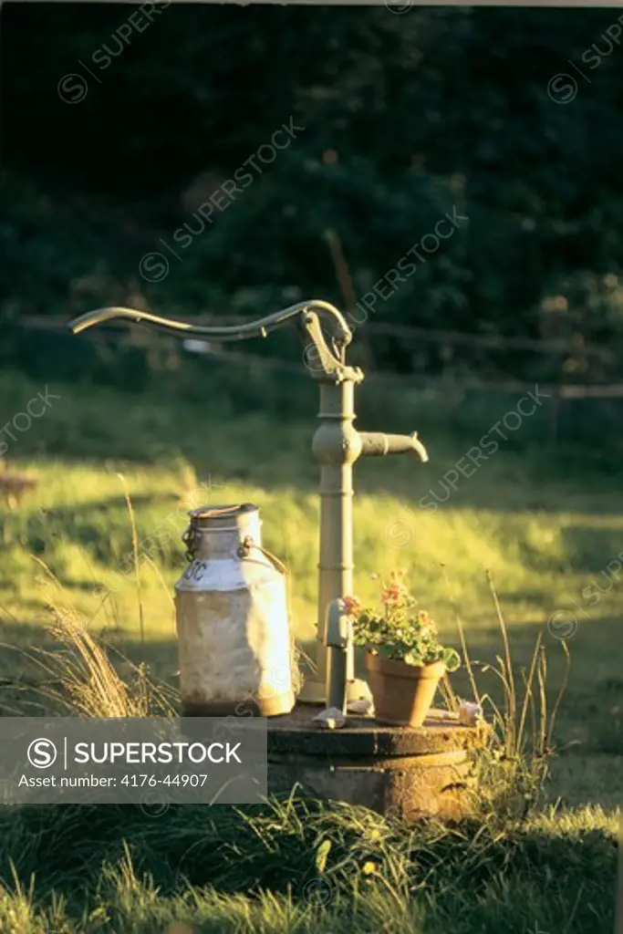 Hand cranked water pump with a metal contaiiner kept aside
