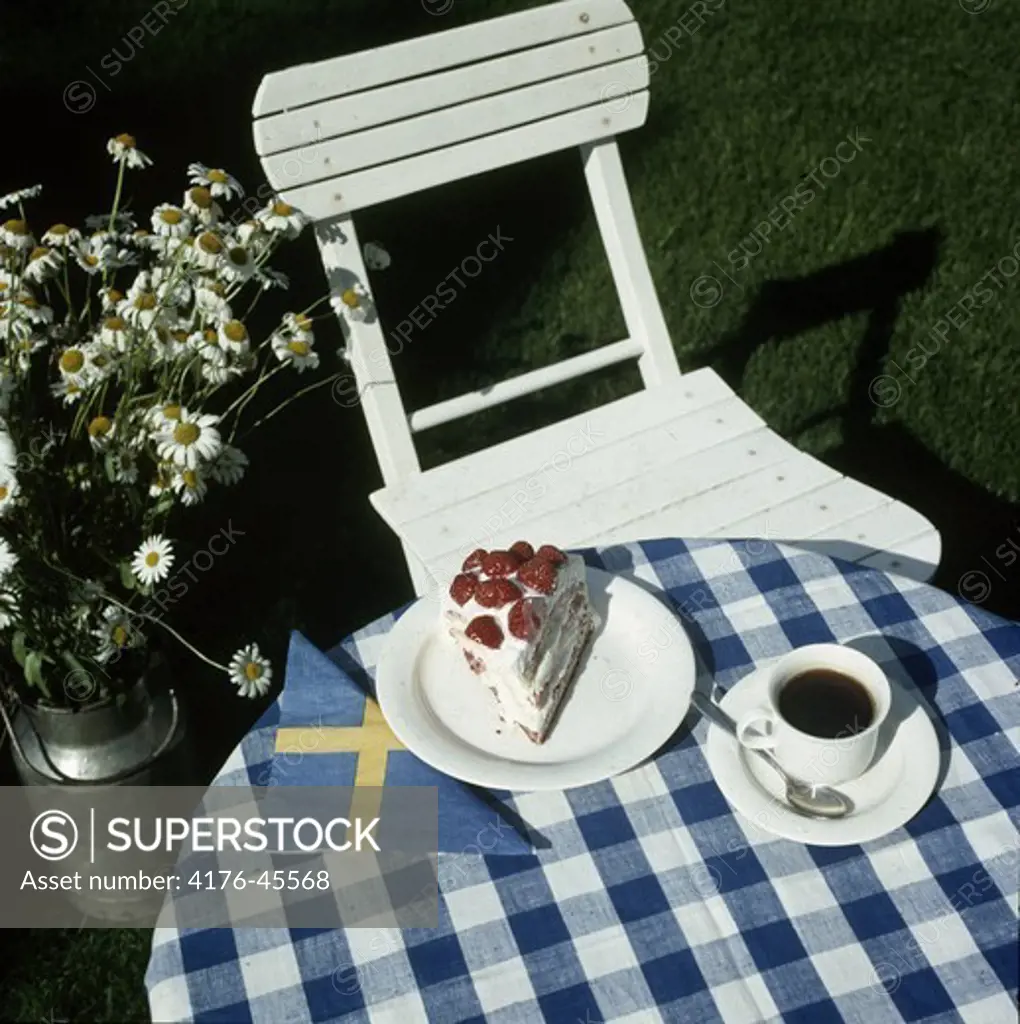 A slice of strawberry cake and a coffee cup on a garden table