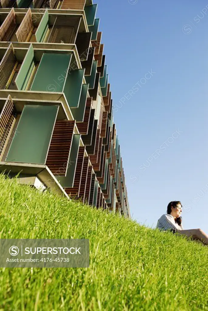 A woman sitting in grass in front of building KILEN in Copenhagen, Denmark.