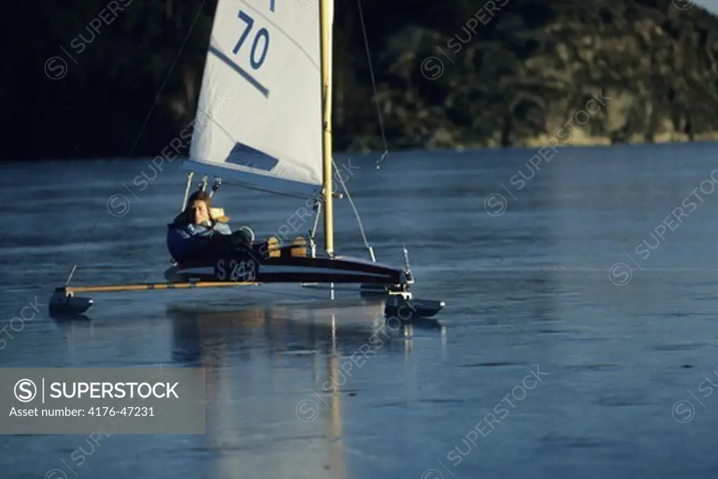 A person gliding on ice in a sleigh with a sail