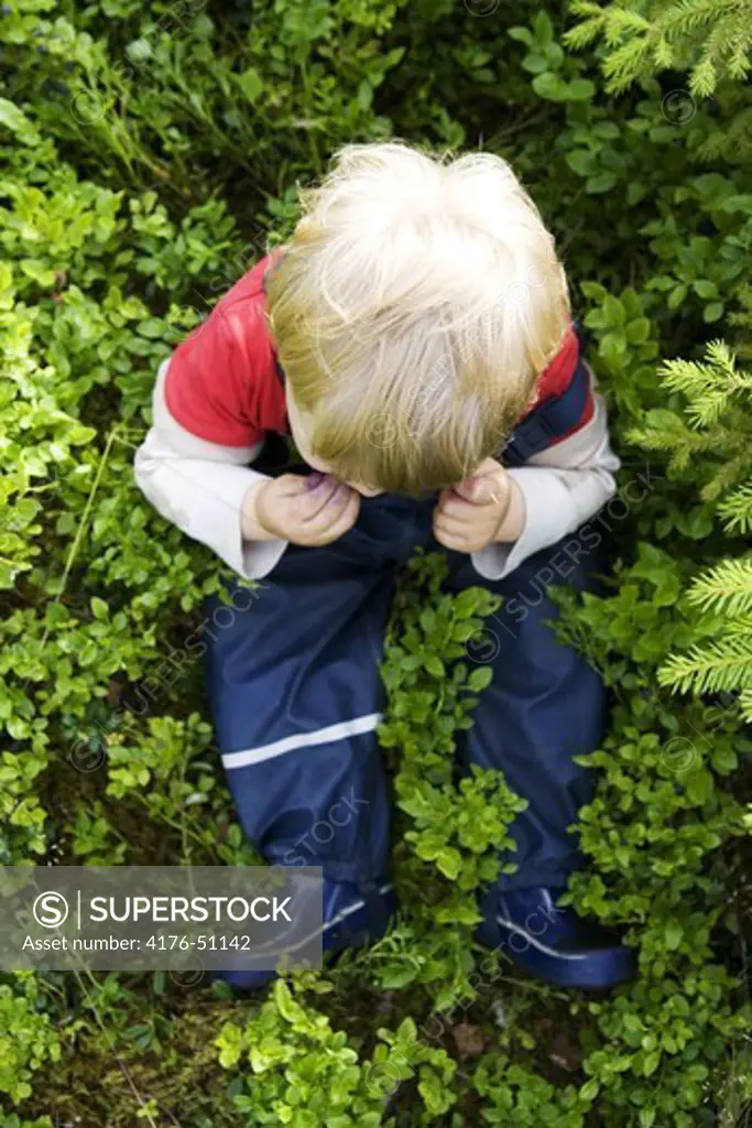 Little boy sitting in grass eating blueberries.
