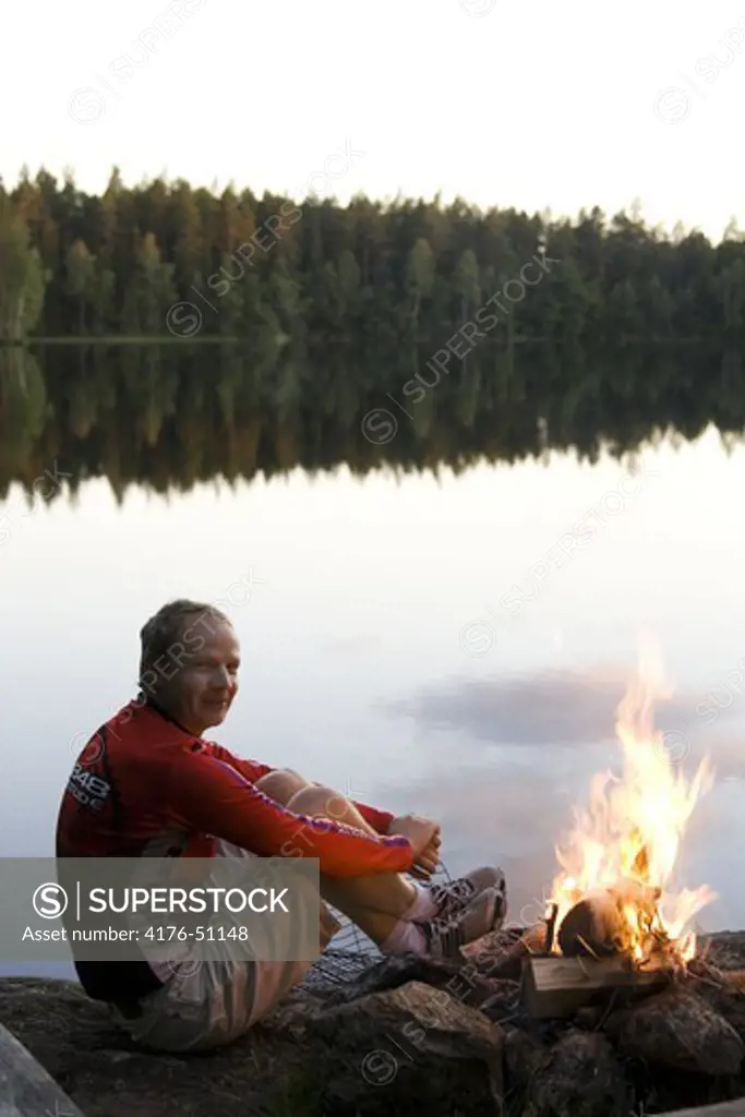 Man sitting in front of a small lake getting warm f