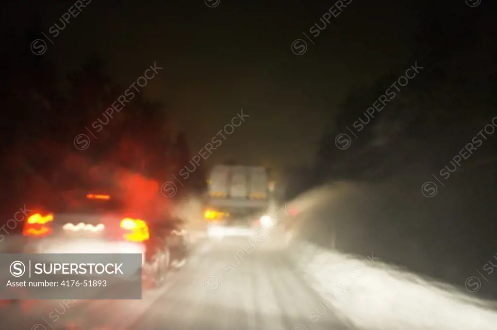 Clearing roads at night after heavy snowfall. Snöröjning av väg i tungt snöfall, bilar och bromsljus.