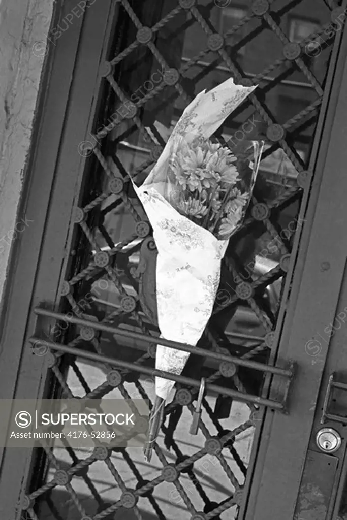 A wrapped bouquet of flowers placed in a door grating.  New York, USA