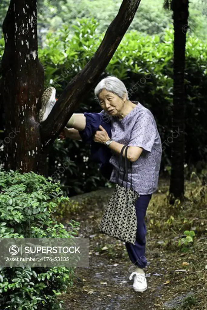 Äldre vig kinesisk kvinna stretchar benet på ett träd