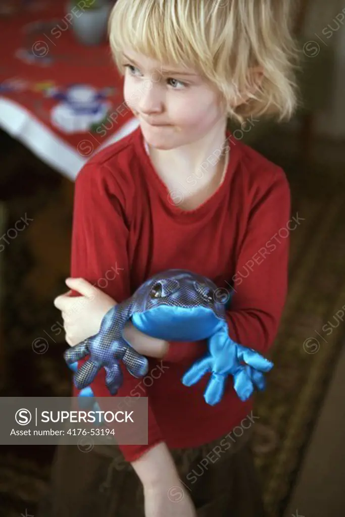 A girl holding a blue toy frog on her arm.