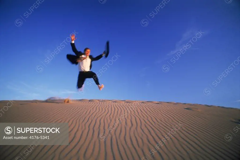 Businessman with briefcase jumping down sand dune