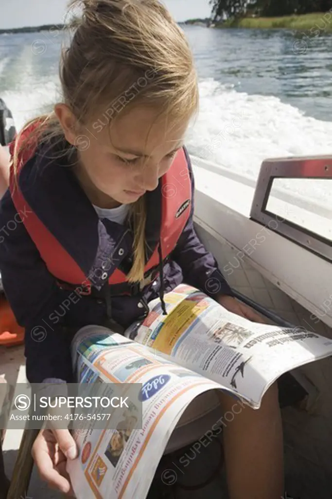 Teenage girl reading a newspaper in a motorboat, Stockholm Archipelago, Sweden