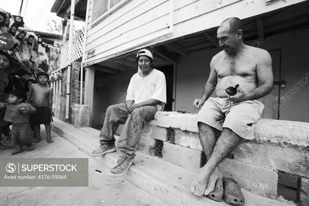 Two men working as salesman on the street, kids in the background, Ambergris Caye, Belize.