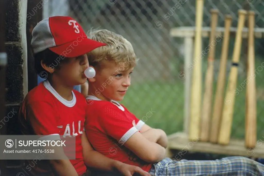 Little leaguers sitting with the baseball bats chewing bubble gum USA