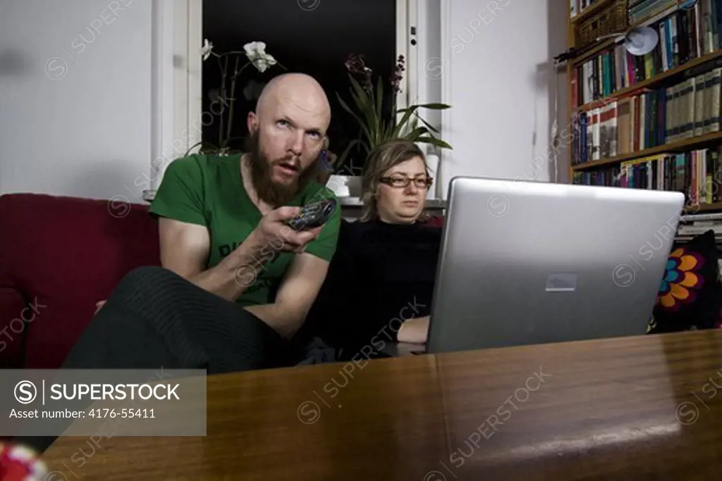 Young man watching TV and a young women using a laptop.