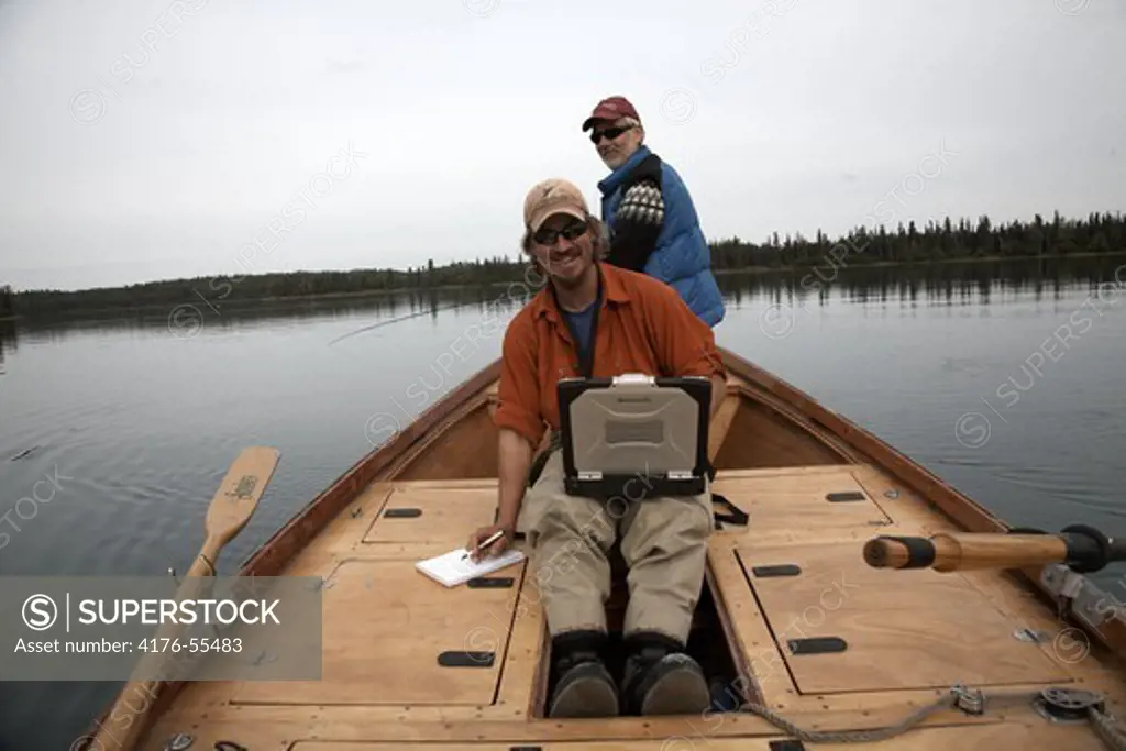 World traveler Dan T Cook is checking his email when Stig Norberg (background) flyfishing. Alaska.