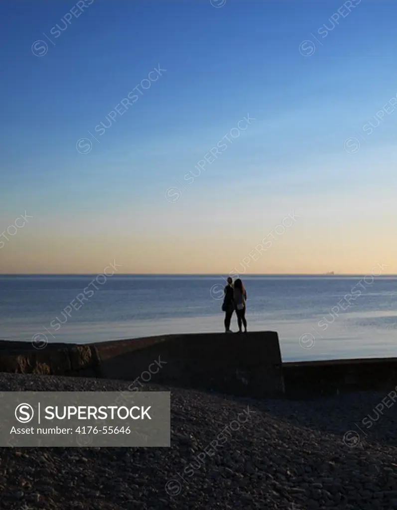 Two girls standing looking out the sea at sunset