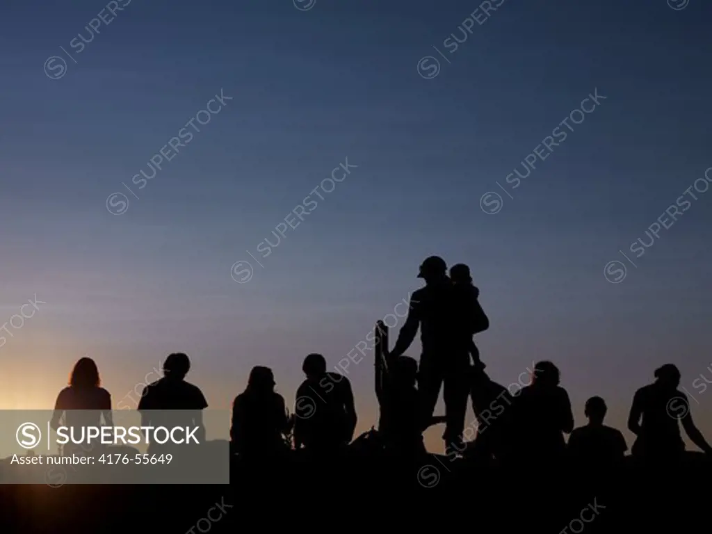 A silhuette picture of some people sitting on the beach at the sunset.