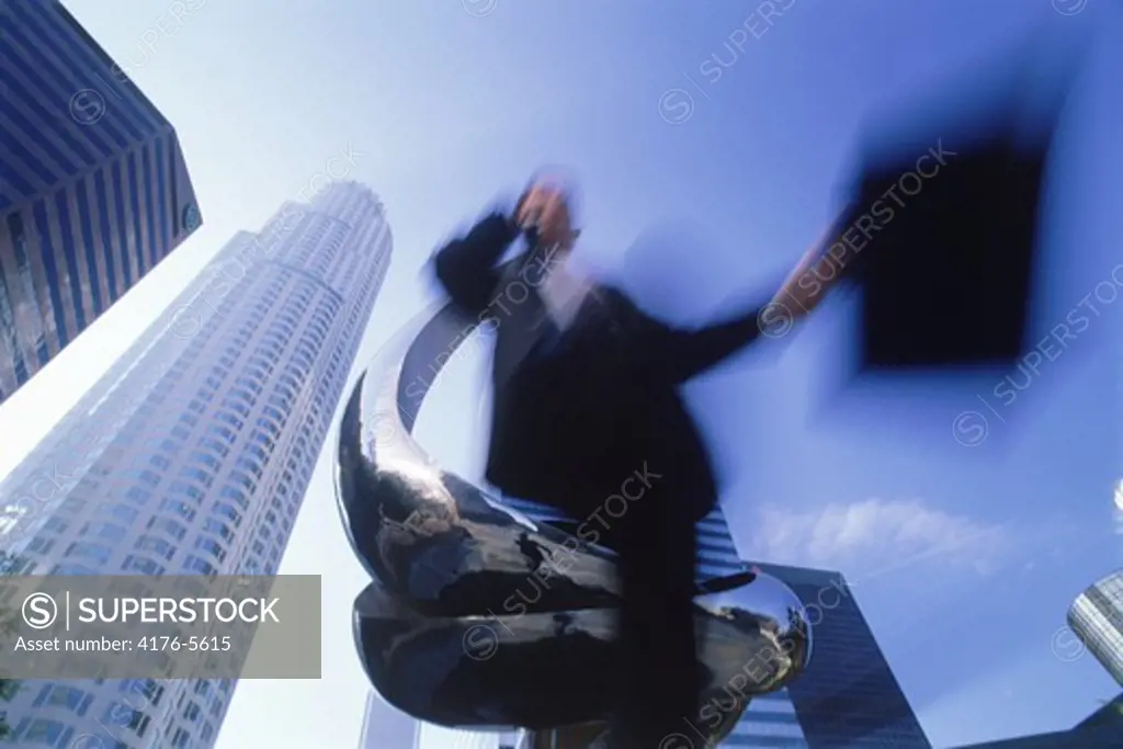 Businessman with briefcase racing past statue amid Los Angeles skyscrapers