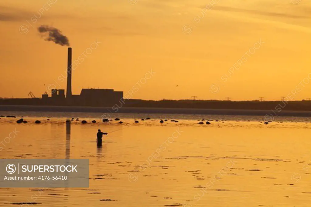 A flyfisherman infront of a industry on the danish eastcoast, Denmark.
