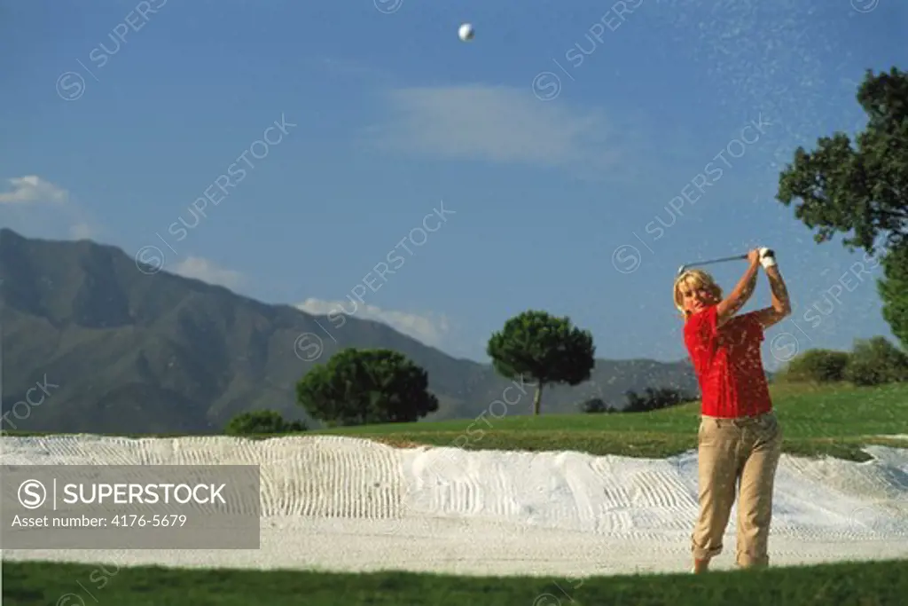 Woman golfer blasting out of sand trap