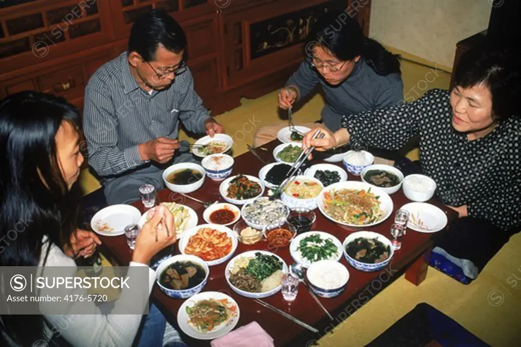 Family sitting at dinner table eating variety home made Korean foods