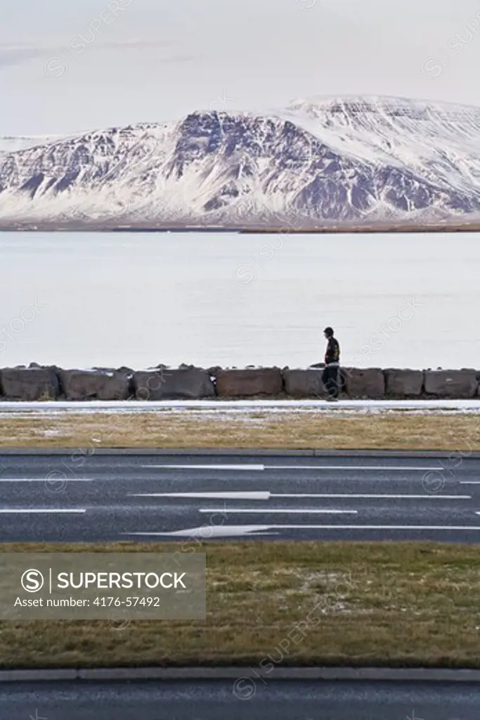 Person walking on a cold afternoon on Saebraut Rd.  Mountain Esja in the background.  Downtown Reykjavik, Iceland.