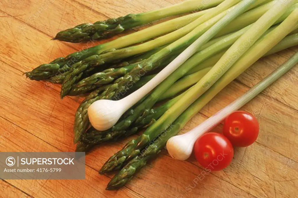 Asparagus with green onions and tomatoes on wooden cutting board