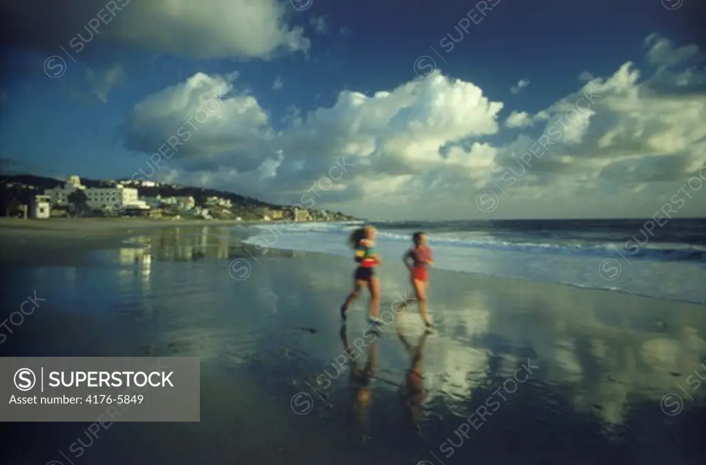 Two woman running along Laguna Beach shore in Southern California at sunset