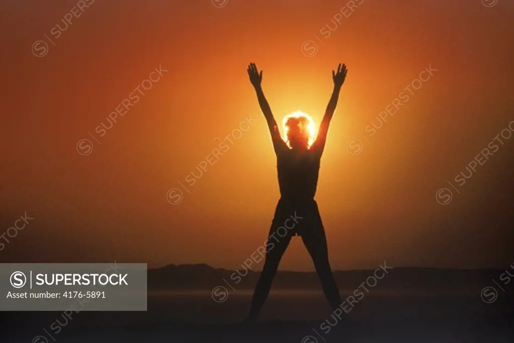 Woman silhouetted by sun in victory posture