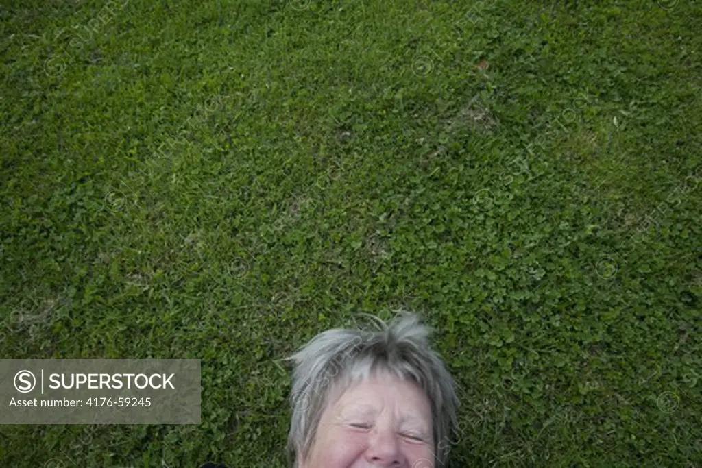 An elderly woman laughing while lying on the grass.