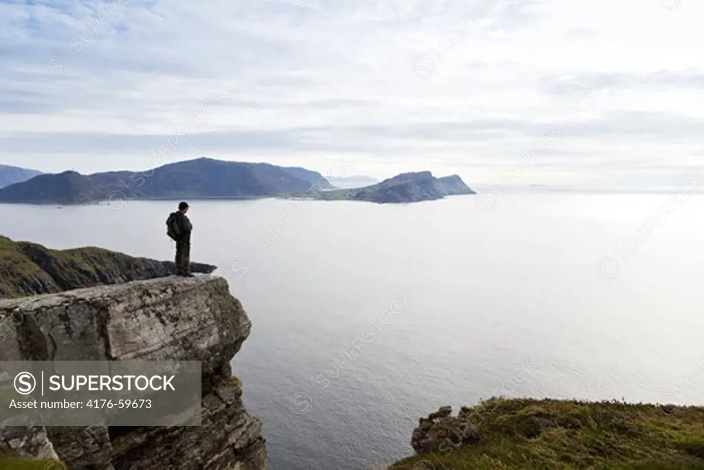 Man standing on a cliff looking out on the open sea,Runde,Norway.